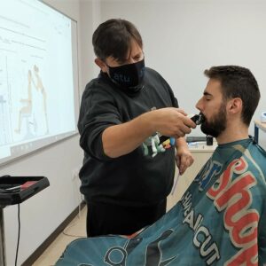 Barbero acicalando la barba de un hombre de cabello oscuro en clase