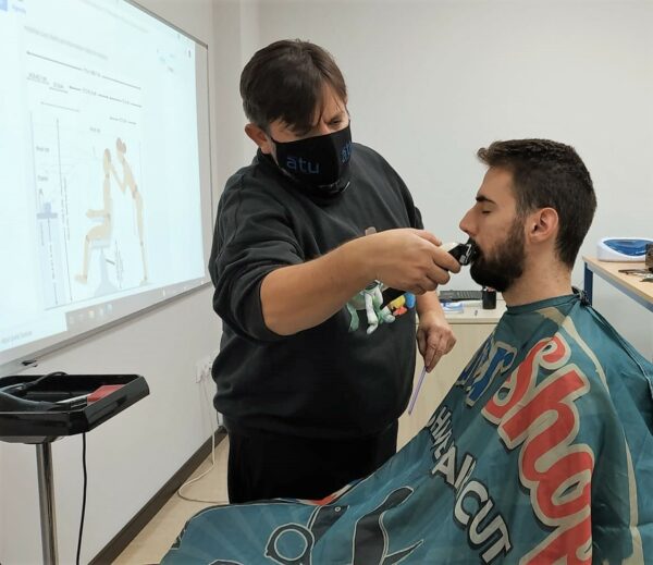 Barbero acicalando la barba de un hombre de cabello oscuro en clase