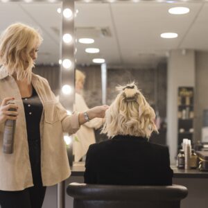 Mujer de espalda con cabello hasta los hombros de color rubio siendo peinada por una peluquera