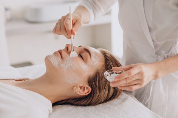 Cosmetóloga haciendo tratamiento facial a una mujer recostada
