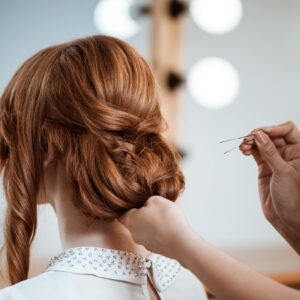 Peluquera haciéndole un peinado con un moño a una mujer pelirroja