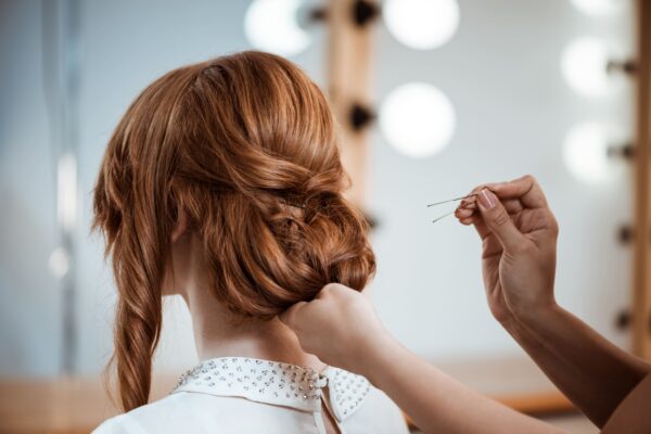 Peluquera haciéndole un peinado con un moño a una mujer pelirroja