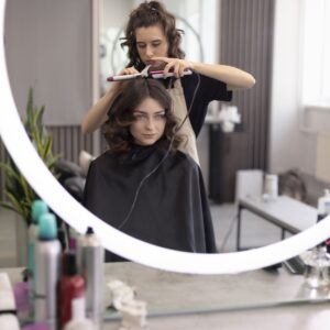 Mujer sentada frente al espejo a la que una peluquera le esta haciendo peinado