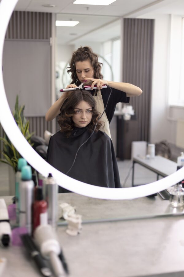 Mujer sentada frente al espejo a la que una peluquera le esta haciendo peinado