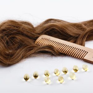 Capsulas de aceite vitaminas junto a cabello marrón y un peine de madera