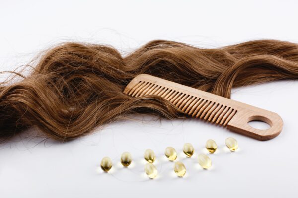 Capsulas de aceite vitaminas junto a cabello marrón y un peine de madera