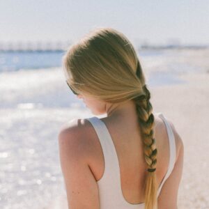 Una mujer rubia sentada en la playa con su cabello atado en forma de una trenzas