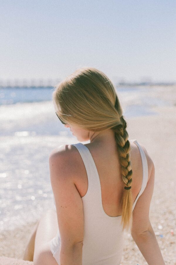 Una mujer rubia sentada en la playa con su cabello atado en forma de una trenzas